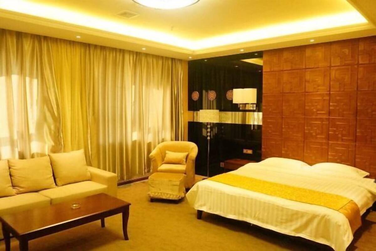Una habitación de hotel con una cama, un sofá, una silla, una mesita de café y una lámpara.