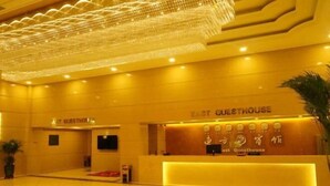 A hotel lobby with a reception desk labeled "East Guesthouse," a chandelier, and a potted plant. - East Guesthouse (Muling)