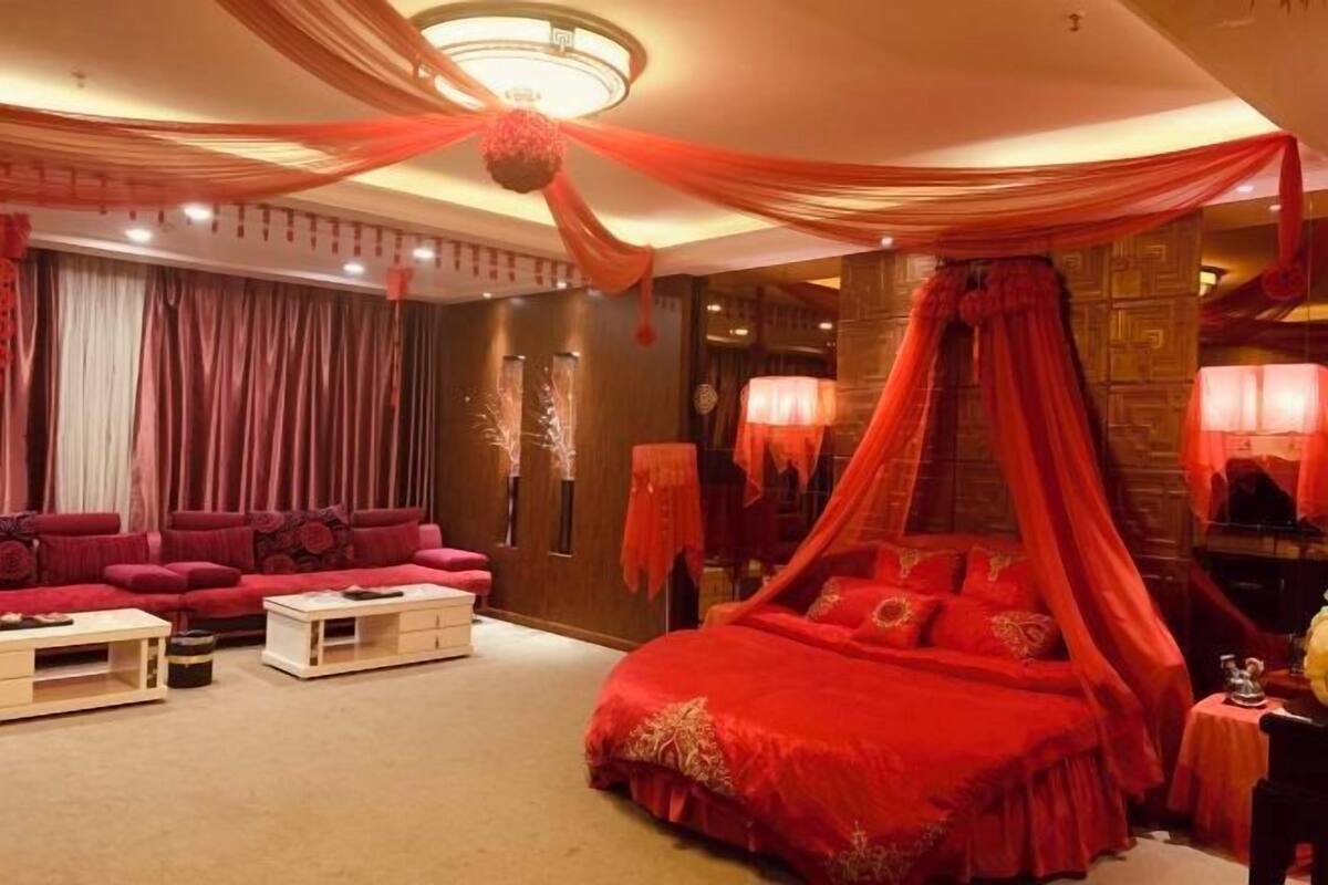 Una habitación con una cama a dosel rojo, un sofá rojo y una mesa de centro blanca.