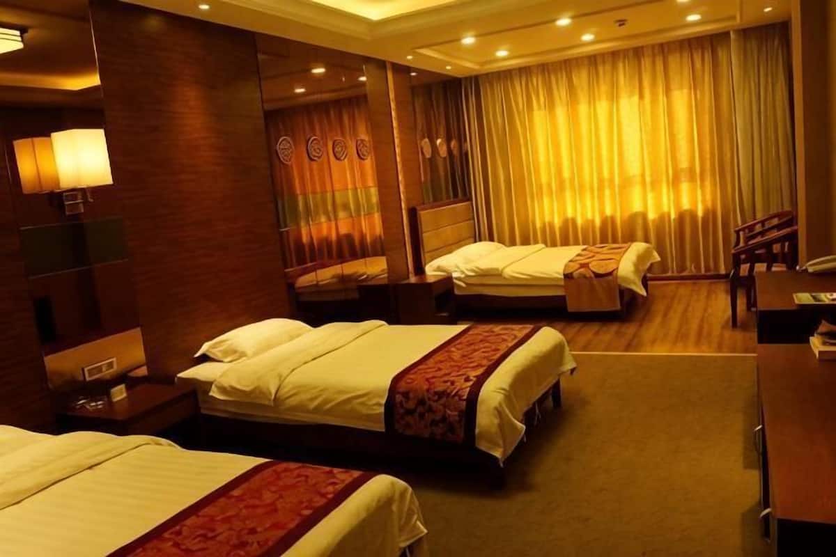 Habitación de hotel con tres camas, un escritorio, una silla y un ventanal con cortinas.
