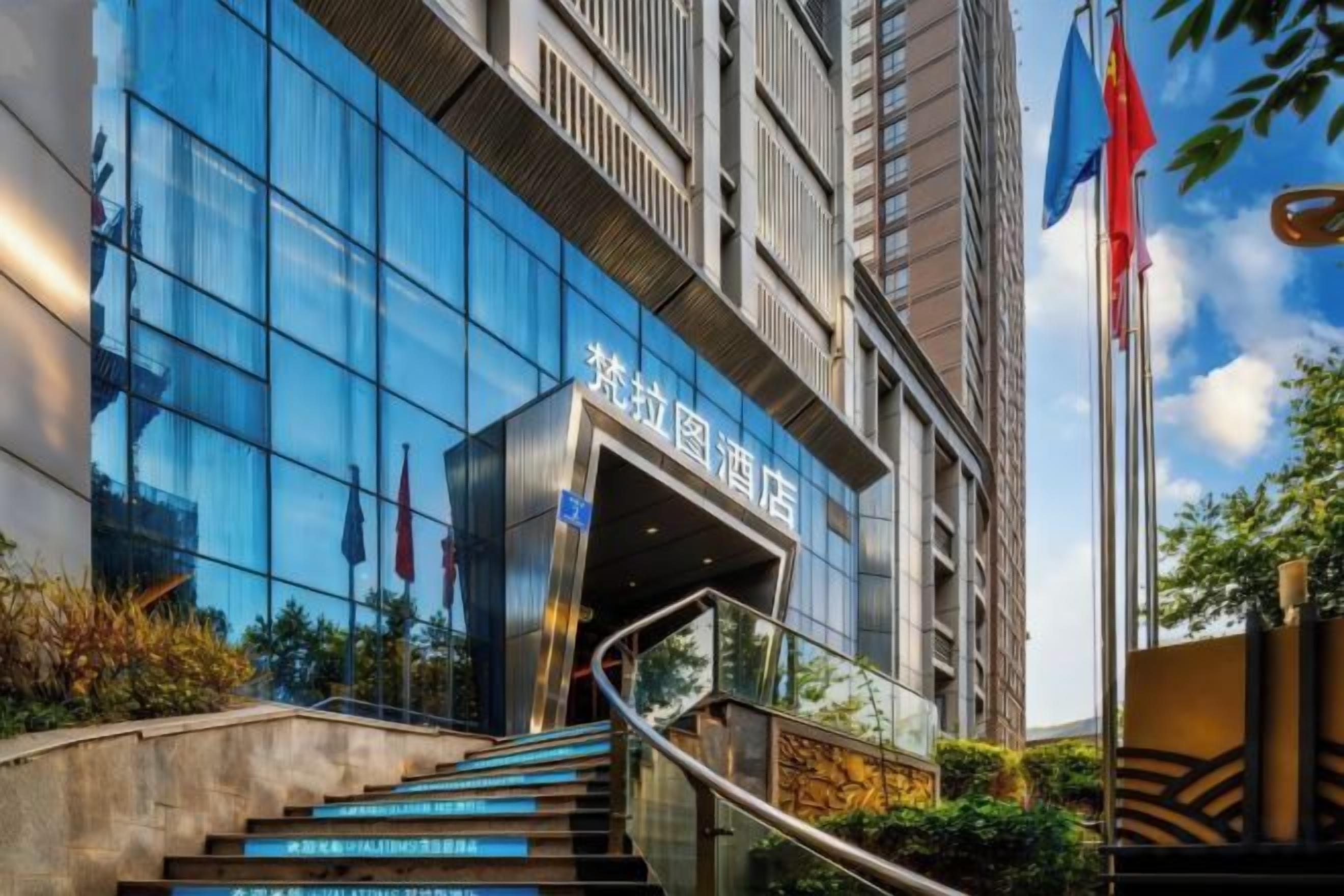 A modern hotel entrance with a glass facade, a staircase leading to the entrance, and flags on poles.