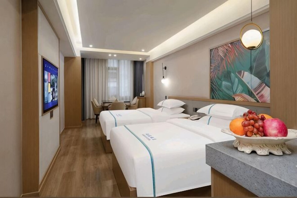 Ett hotellrum med två sängar, ett skrivbord, en stol, en tv och en fruktskål.