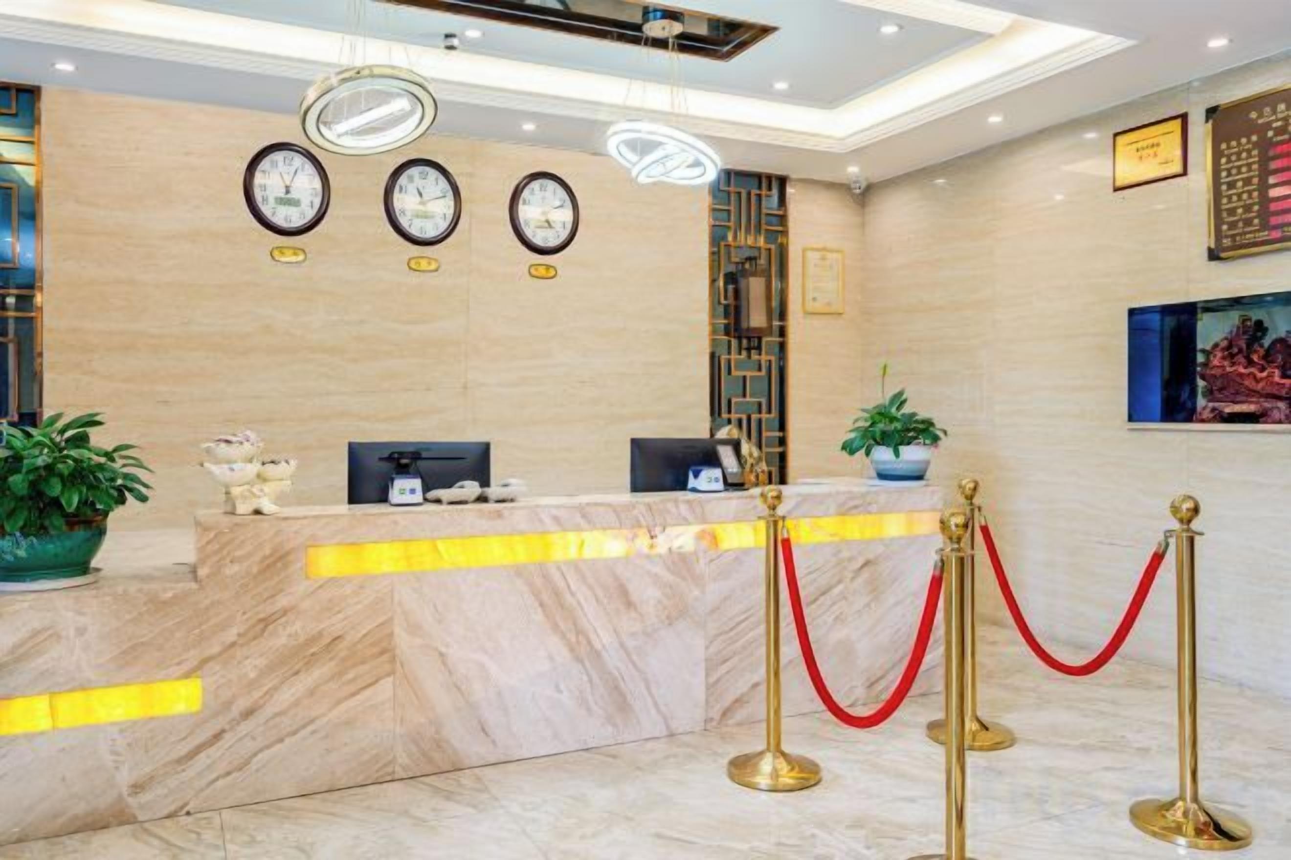 A hotel reception area with marble counters, clocks, and a red rope barrier.