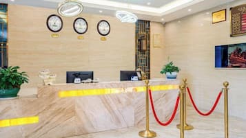 A hotel reception area with marble counters, clocks, and a red rope barrier.
