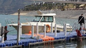 Ein Boot liegt an einem Steg mit einer felsigen Küstenlinie und Gebäuden im Hintergrund.