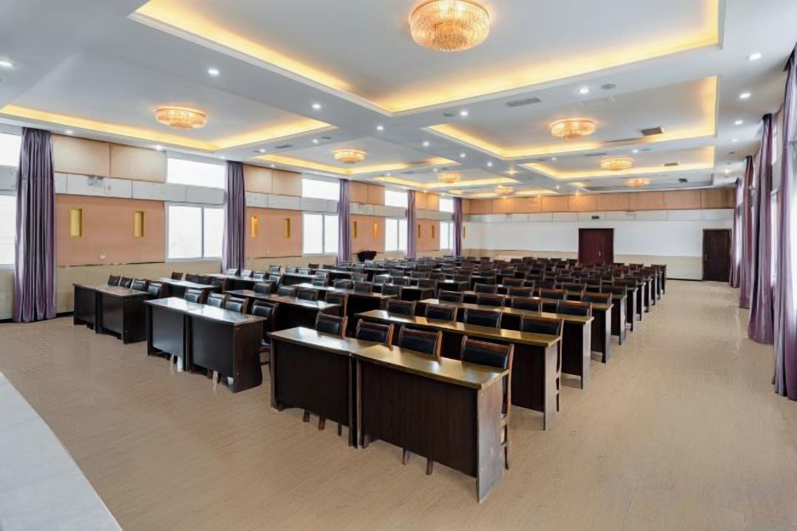 A conference room with rows of tables and chairs, large windows, and a modern chandelier.