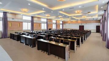A conference room with rows of tables and chairs, large windows, and a modern chandelier.