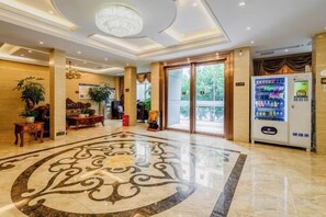 Rebedor d'hotel amb sòl de marbre, una làmpada penjant, taulell de recepció i màquina expenedora.
