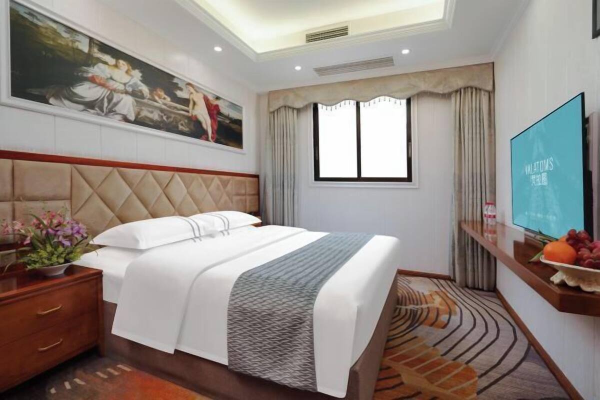 Une chambre d’hôtel avec un grand lit, un tableau au mur, une télévision et une fenêtre avec des rideaux.