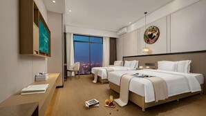 Ein Hotelzimmer mit zwei Betten, einem Schreibtisch, einem Fernseher und einem großen Fenster mit Blick auf die Stadt.