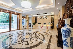 Un vestíbulo de hotel con una recepción, un jarrón decorativo grande y un suelo con estampado.