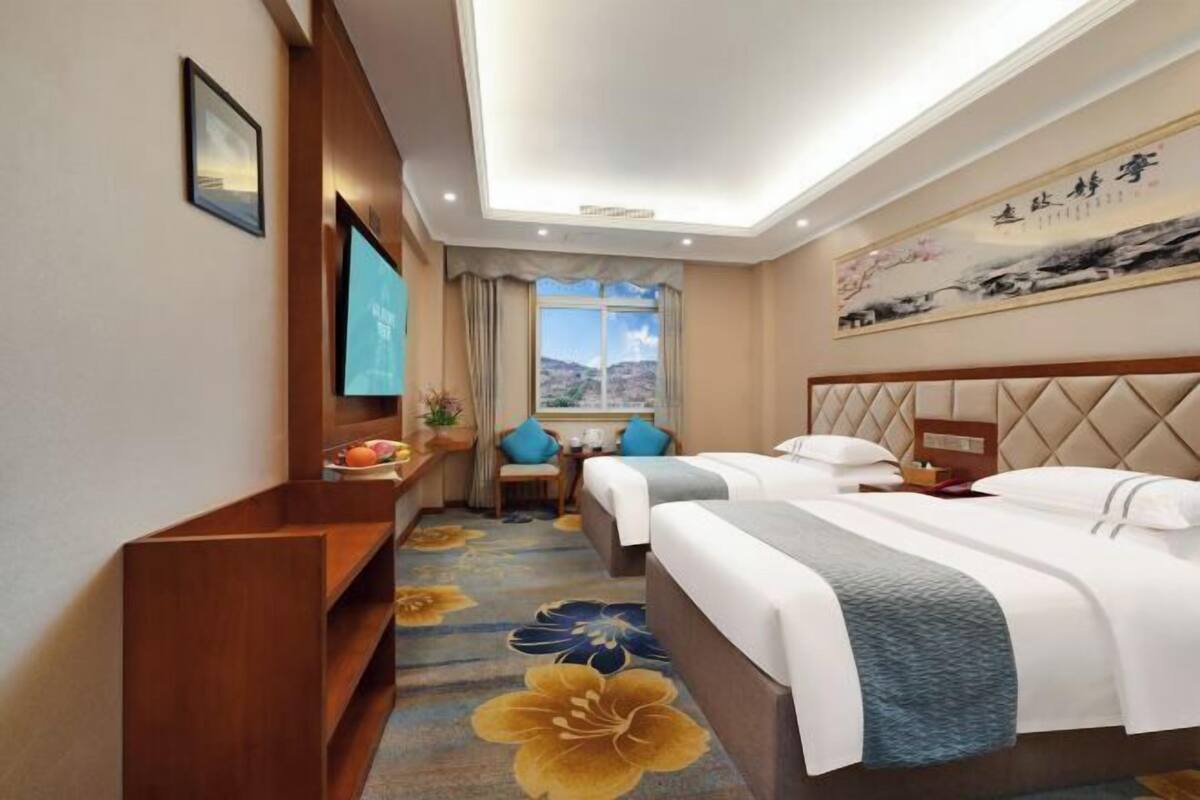 Une chambre d’hôtel avec deux lits, une télévision, un bureau avec une chaise et une fenêtre donnant sur les montagnes.