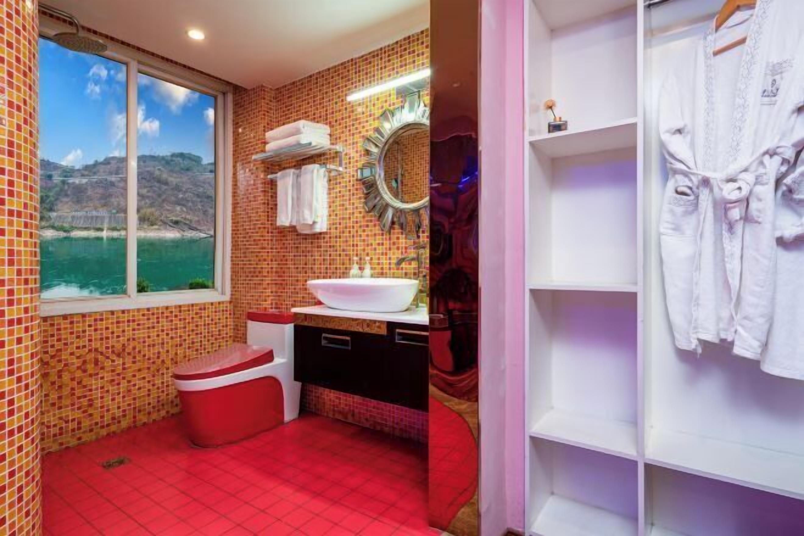 A bathroom with a red floor, a white sink, a mirror, and a window with a view of a body of water.