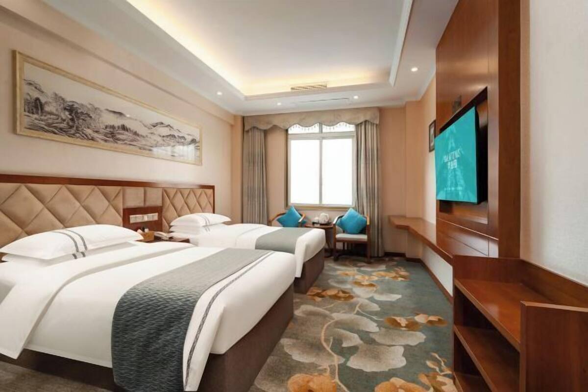Une chambre d’hôtel avec deux lits, une télévision, un tableau et une fenêtre avec des rideaux.