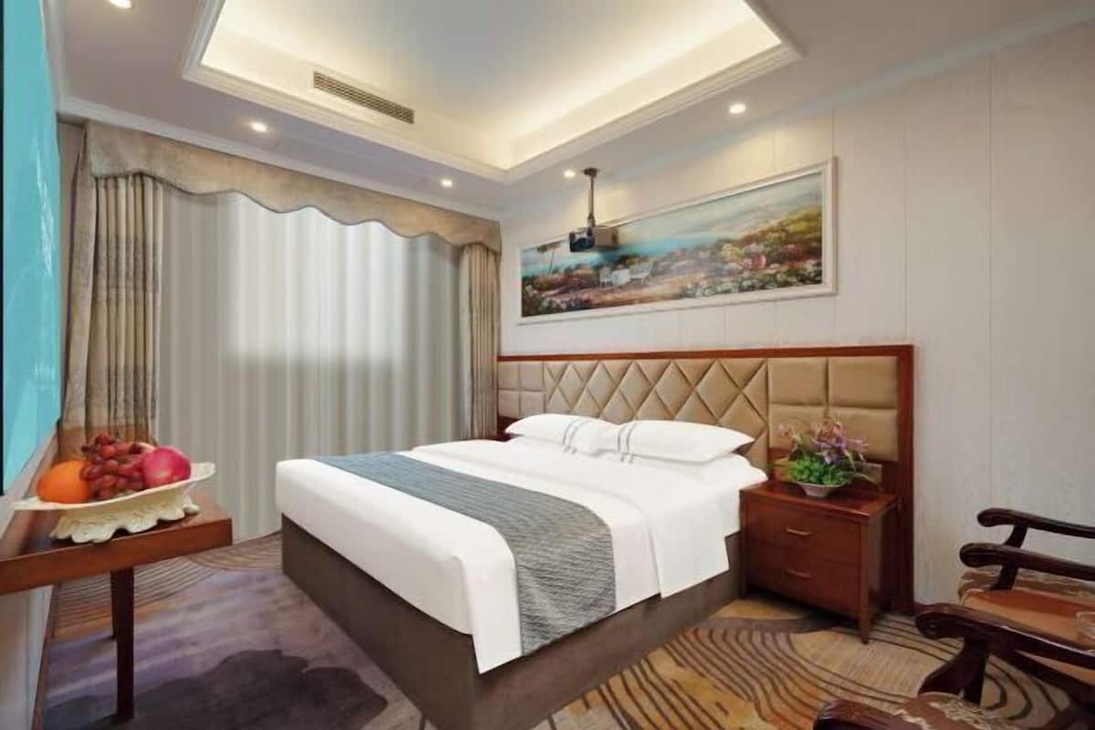 Une chambre d’hôtel avec un lit, une table de chevet avec des fruits, une commode, un banc, un tableau au mur et un luminaire au plafond.