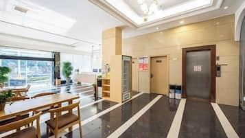 A hotel lobby with a reception desk, a vending machine, and a staircase leading to an elevator.