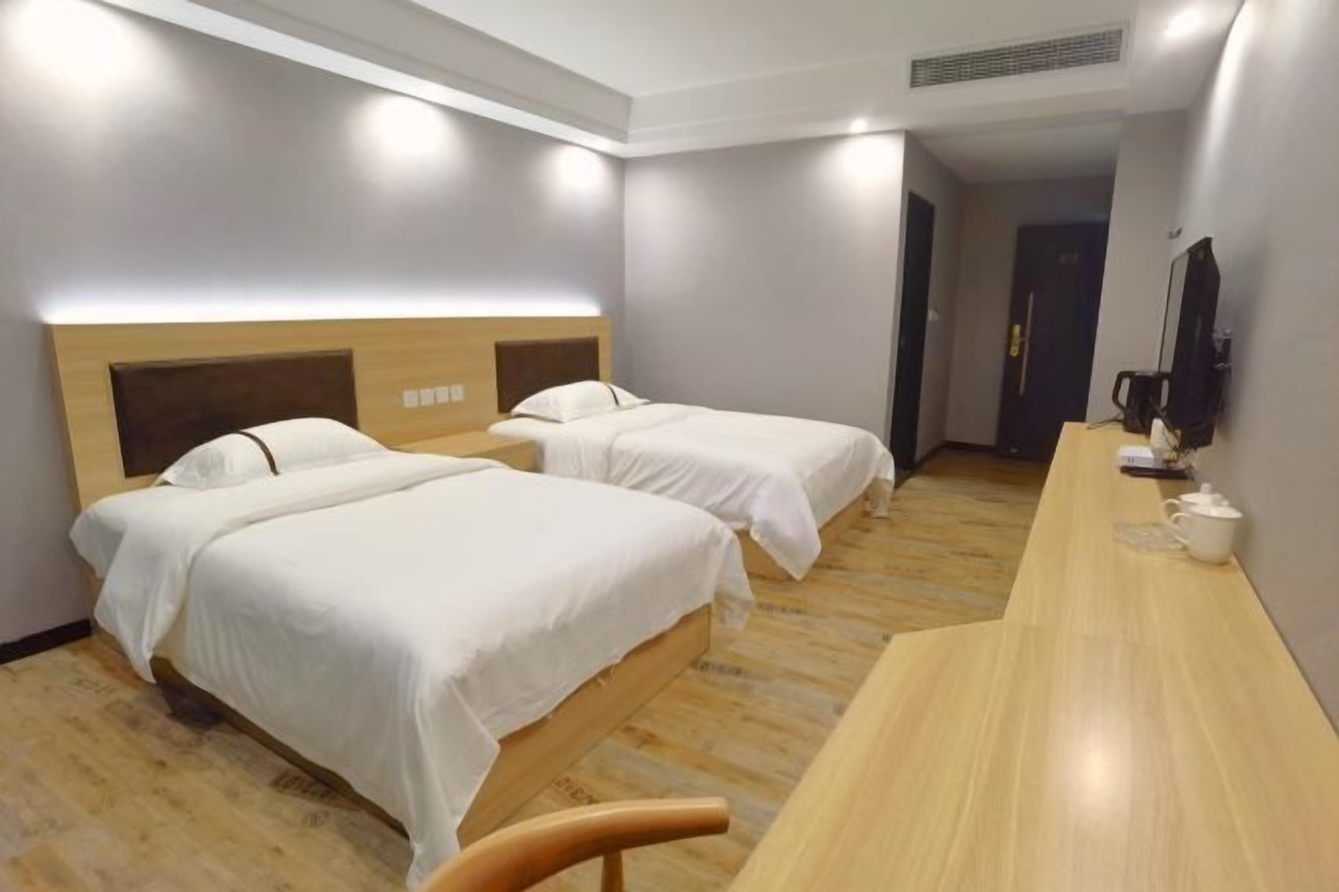 A hotel room with two beds, a wooden desk, and a television on the wall.