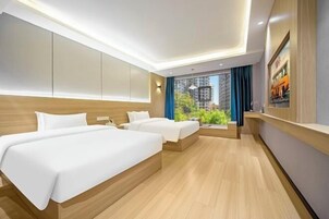 Quarto de hotel moderno com duas camas, uma janela grande com vista para edifícios e uma obra de arte pendurada na parede.