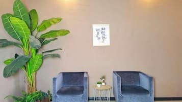Una habitación con dos sillones grises, una mesita redonda con una planta, y una planta verde grande contra la pared.