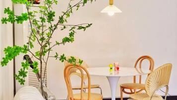 A dining area with a round table, four wooden chairs, a hanging light fixture, and a decorative plant with green leaves.