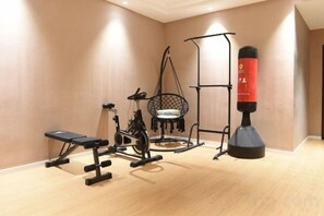 A room with a wooden floor, a stationary bike, a bench, a hanging chair, and a punching bag. - starhao hotel (Xiushan County)