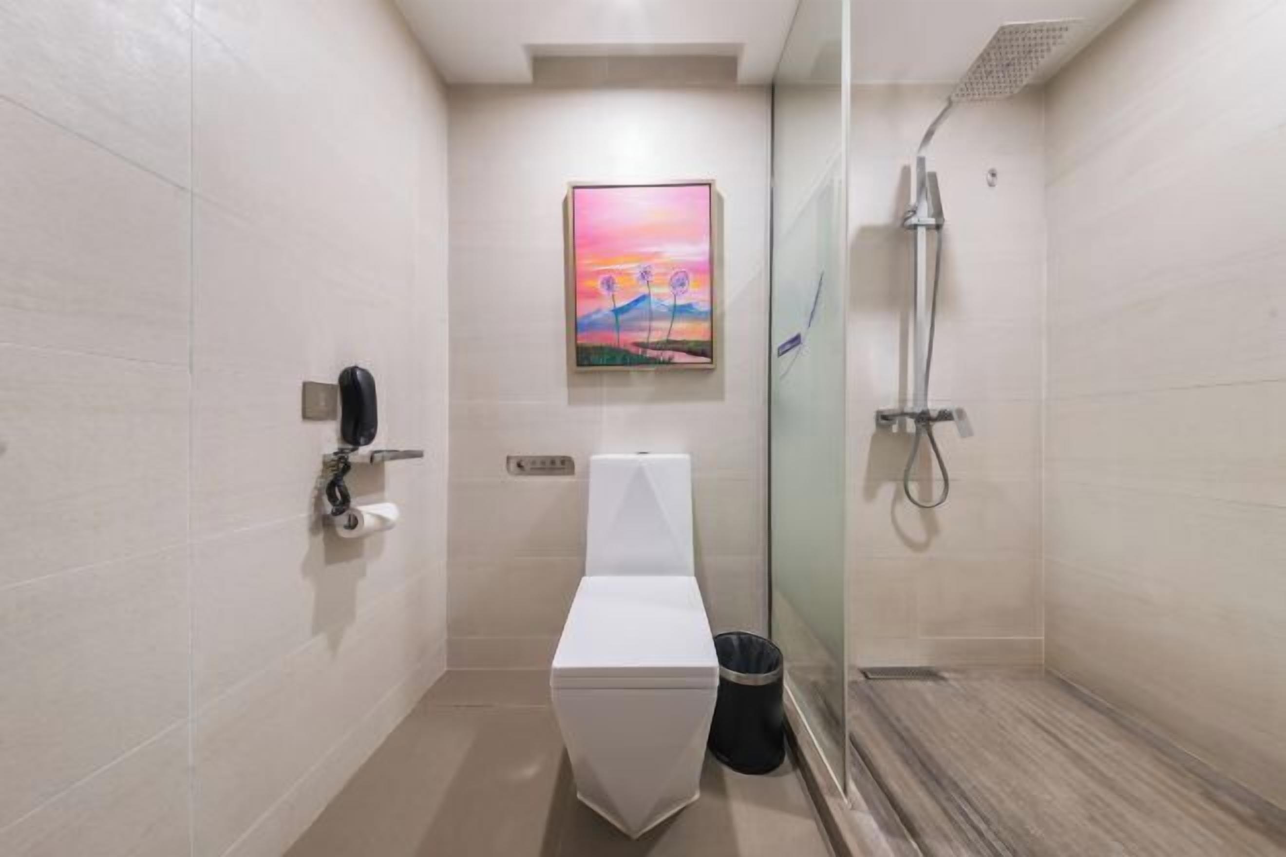 A modern bathroom with a toilet, a glass shower enclosure, and a painting on the wall.