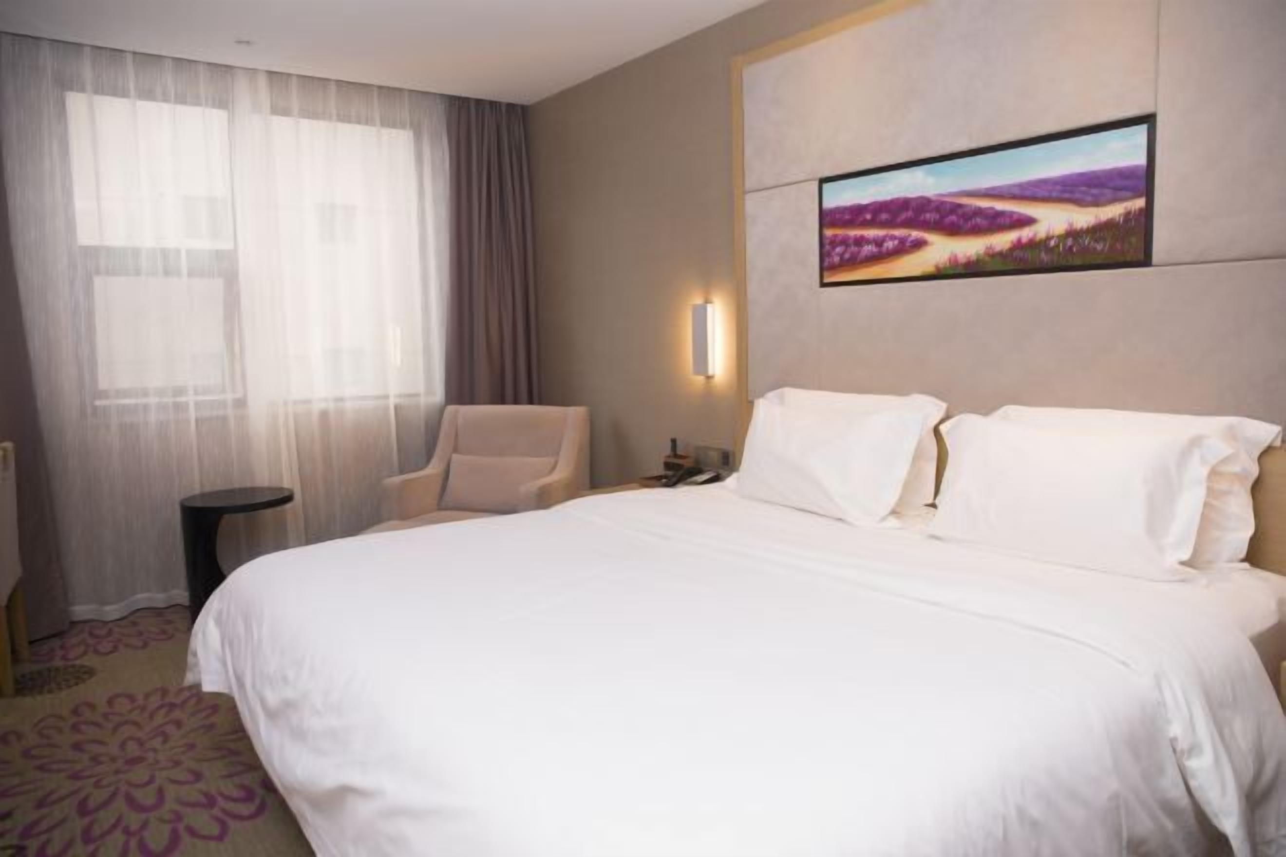 Una habitación de hotel con una cama grande, una silla, una mesita y un cuadro en la pared.