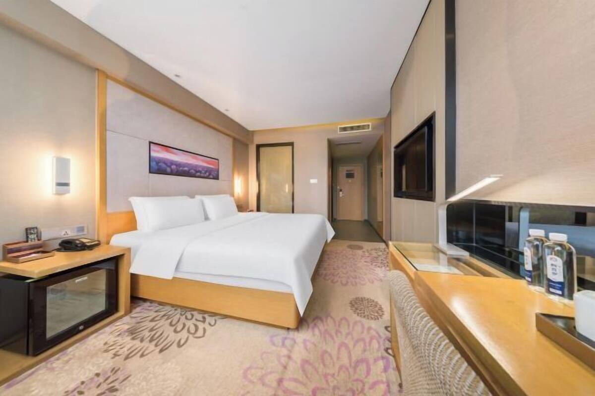 A hotel room with a bed, bedside table, TV, and a view of the hallway.