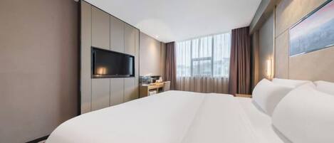 A hotel room with a large bed, a flat-screen TV mounted on the wall, a desk with a chair, and a window with curtains.