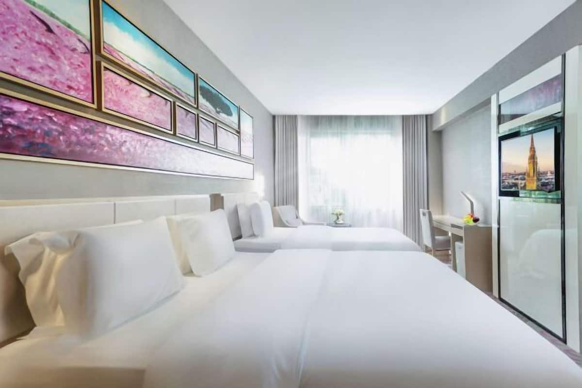 A hotel room with two beds, a desk, a chair, and a large window with a view.