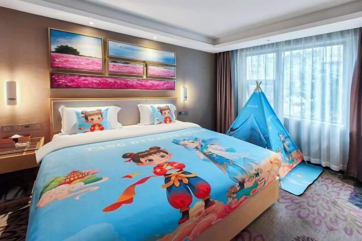 A hotel room with a bed, artwork on the wall, a window with curtains, and a tent-like structure.