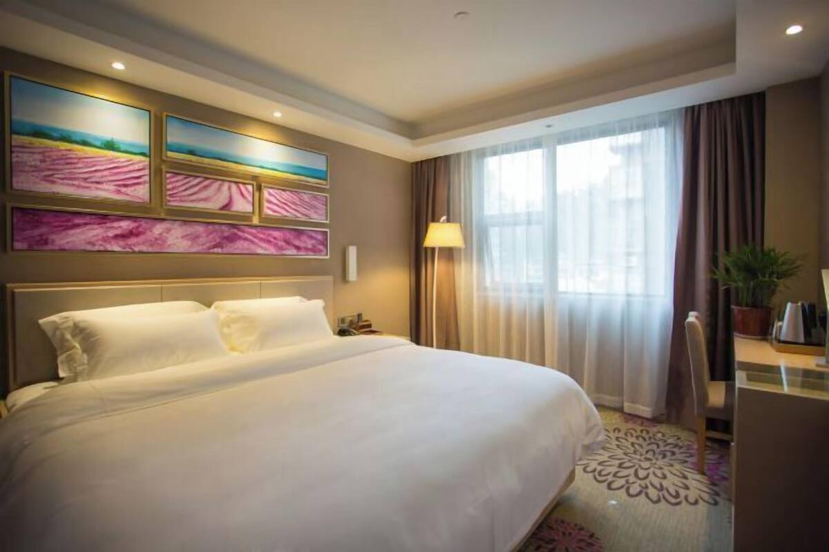 A hotel room with a large bed, a desk, a chair, a lamp, and a window with curtains.