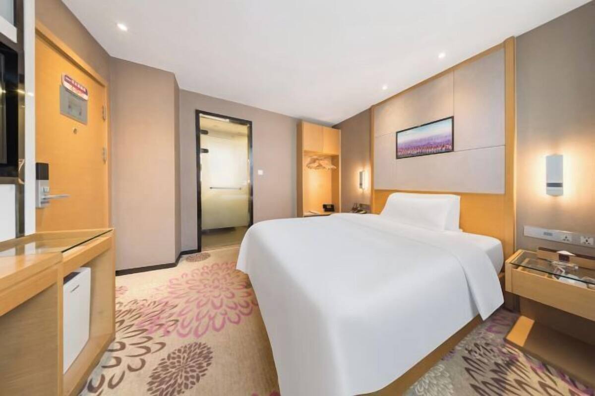 A hotel room with a bed, a desk, a chair, a television, and a wall-mounted light.