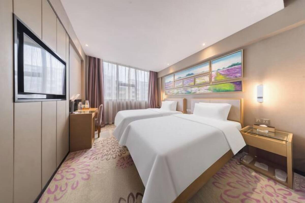 A hotel room with two beds, a TV, a desk, and a painting on the wall.