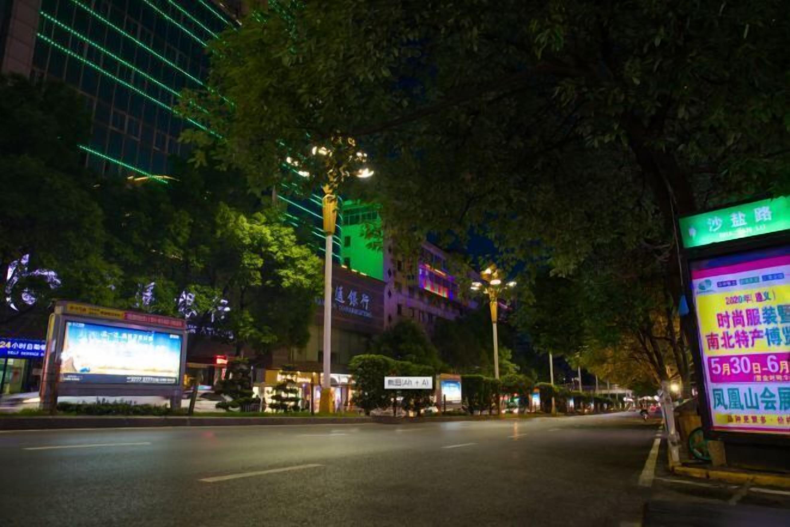 Une scène de rue nocturne avec des bâtiments et des panneaux publicitaires illuminés.
