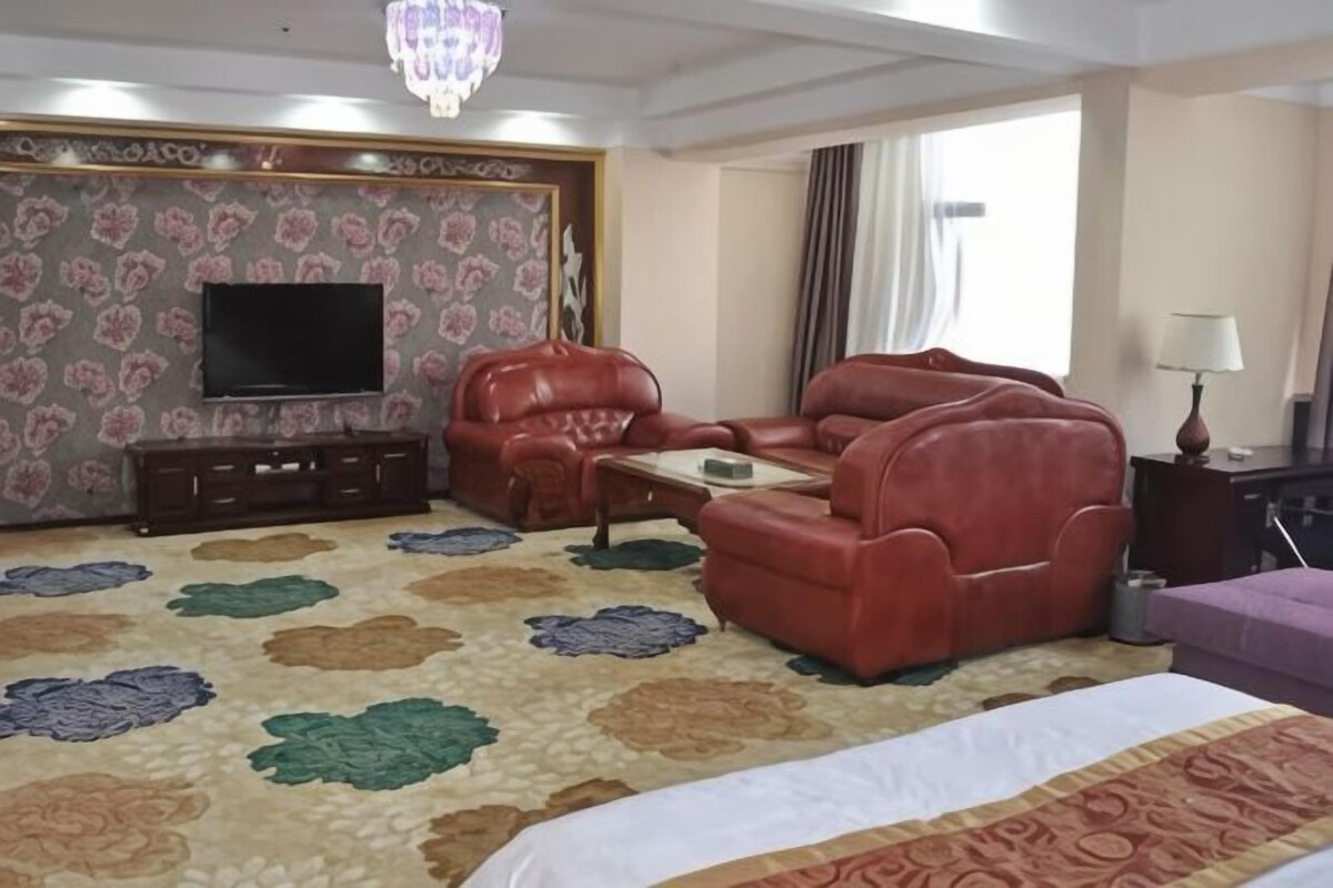 A hotel room with a large bed, a red leather sofa, a television, and a patterned carpet.