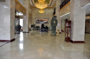 A lobby with a marble floor, a chandelier, a reception desk, and a large painting.