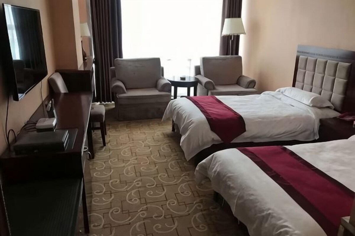 A hotel room with two beds, a desk, a chair, a TV, and a small table.