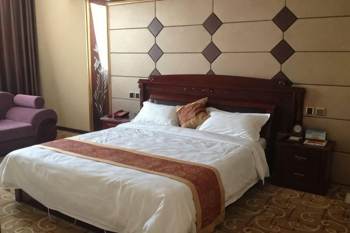 A hotel room with a large bed, a nightstand, a chair, and a decorative wall panel.