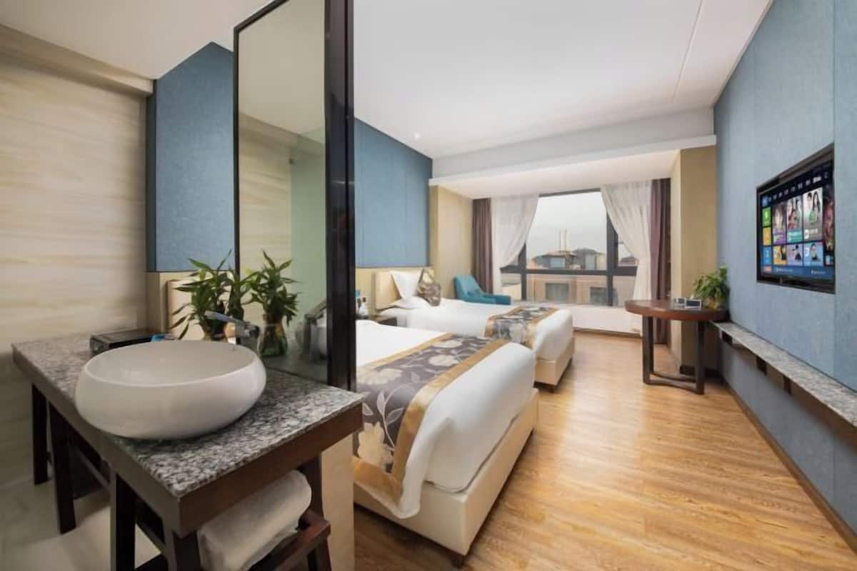 A modern hotel room with a large bed, a bedside table, a bathroom with a sink, and a large window.