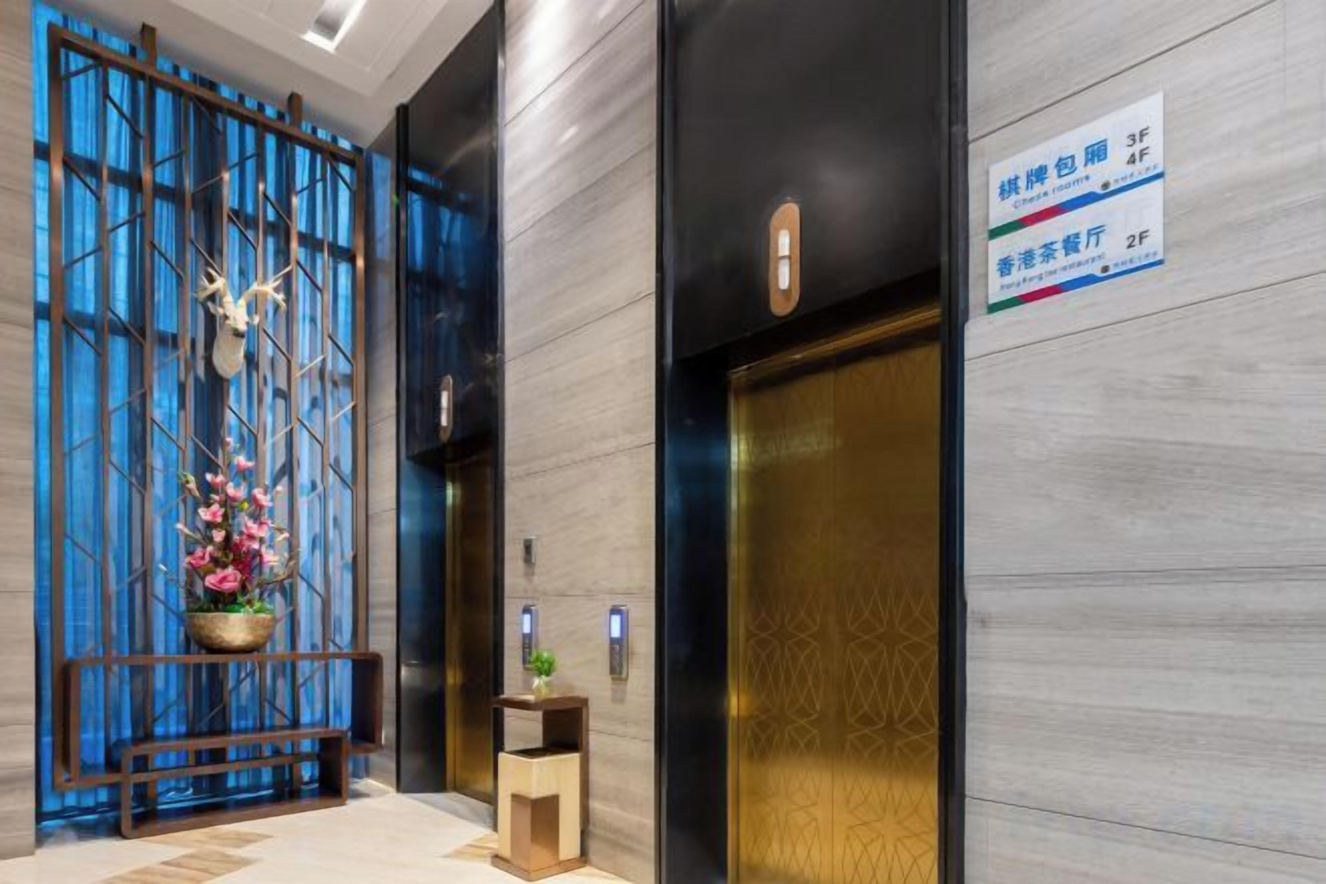 Um hall de hotel com balcão de recepção, divisória decorativa azul e elevador.