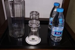 Un plateau avec une carafe en verre, deux verres transparents, une petite bouteille et une bouteille d’eau.