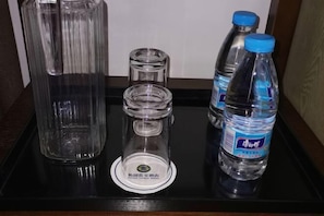 A tray with a tall glass container, a smaller glass container, a bottle of water, and a bottle with a blue cap.