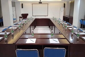 Une salle de conférence avec une longue table, des chaises, des bouteilles d’eau et un écran de projection.