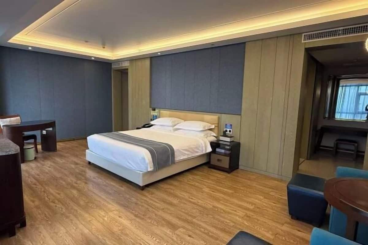 A modern hotel room with a large bed, bedside tables, a desk, and a seating area.