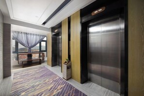 Un vestíbulo de hotel con un ascensor grande, un banco, una planta y una alfombra estampada.