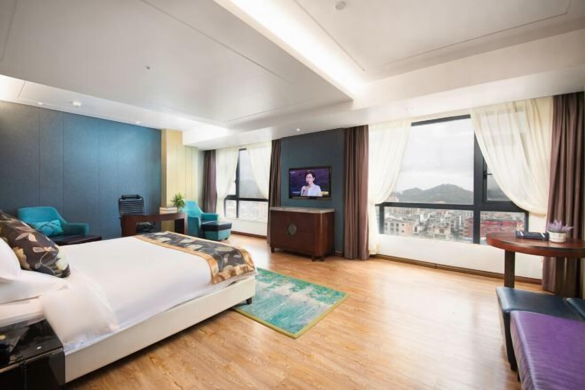 Hotelkamer met een bed, een televisie, een bureau, een stoel en uitzicht op een stadsbeeld.