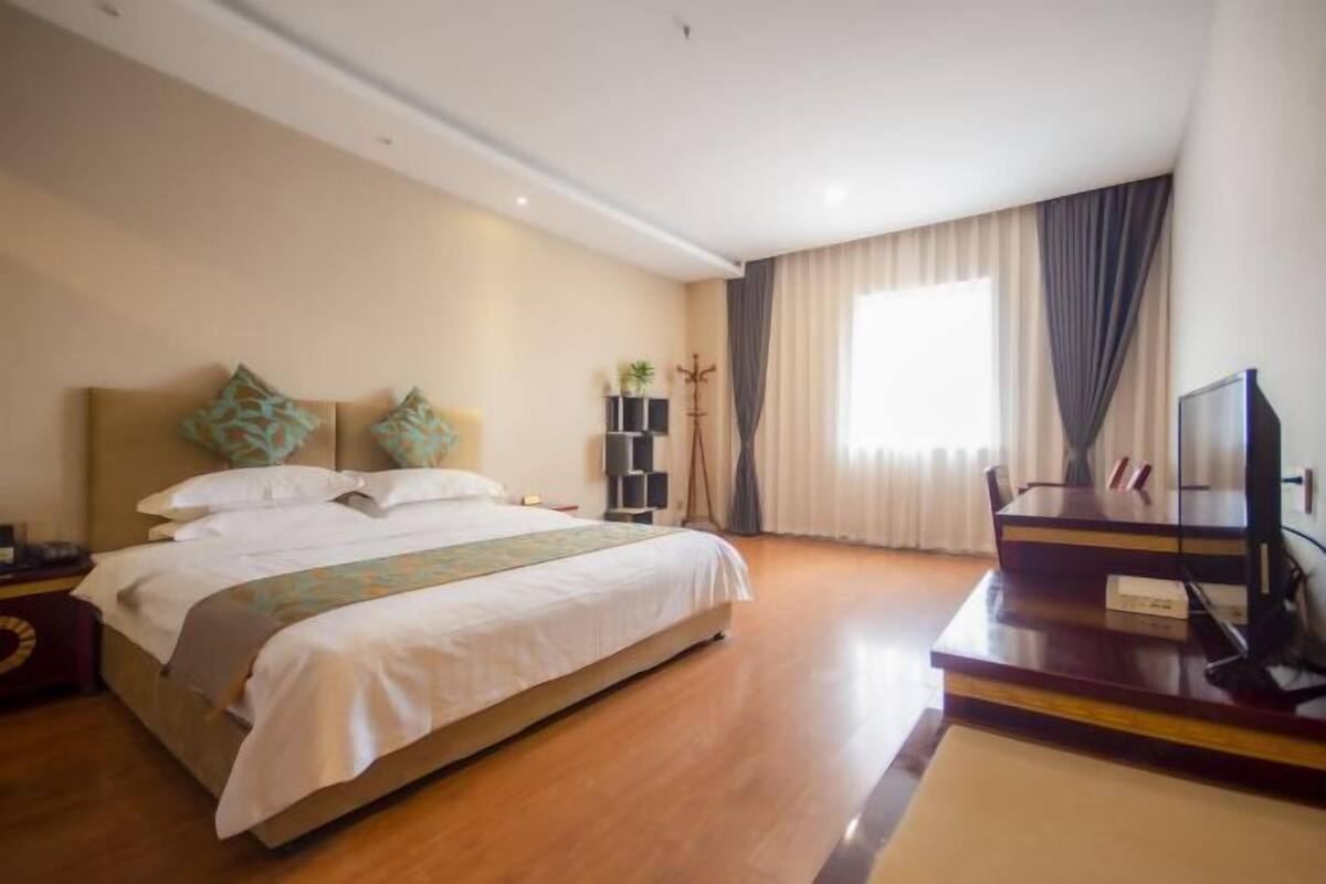 A hotel room with a bed, a TV, a desk, and a window with curtains.