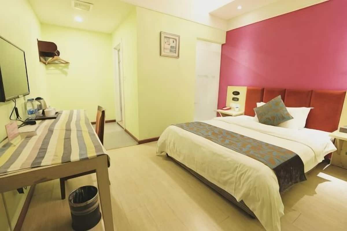 A hotel room with a bed, bedside table, chair, and a desk with a computer.