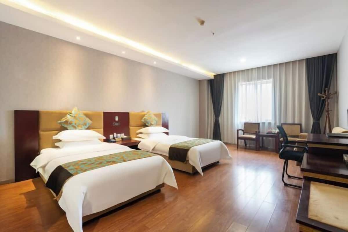 A hotel room with two beds, a desk, a chair, and a large window with curtains.